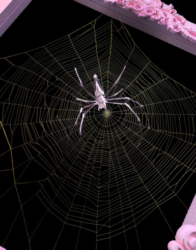A metallic pink spider rests in the middle of a large golden web
